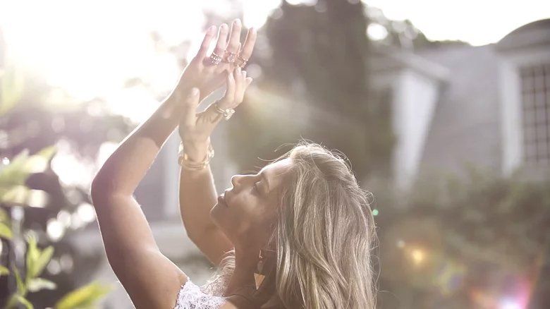 Uma mulher está parada em frente a um prédio com as mãos para cima.