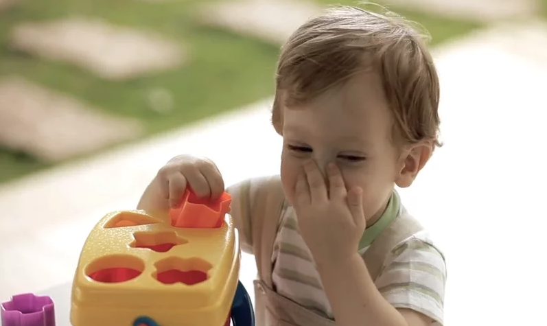 Um bebê está brincando com um brinquedo e cobrindo o nariz.