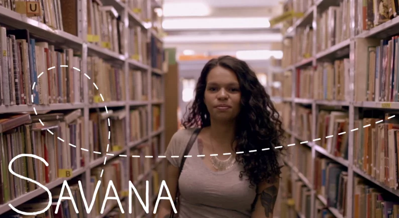 Uma mulher está em uma biblioteca cercada por estantes.