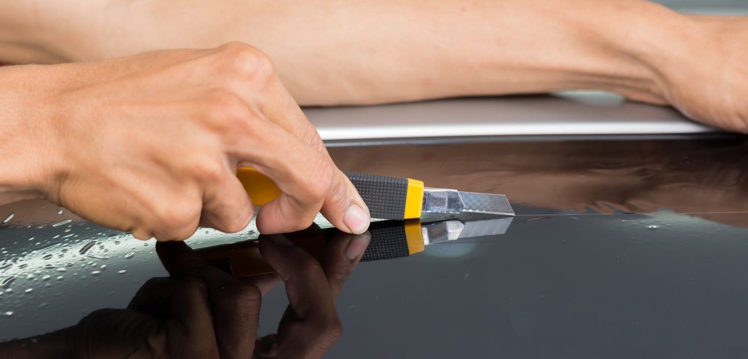 A person is cleaning a car windshield with a scraper.