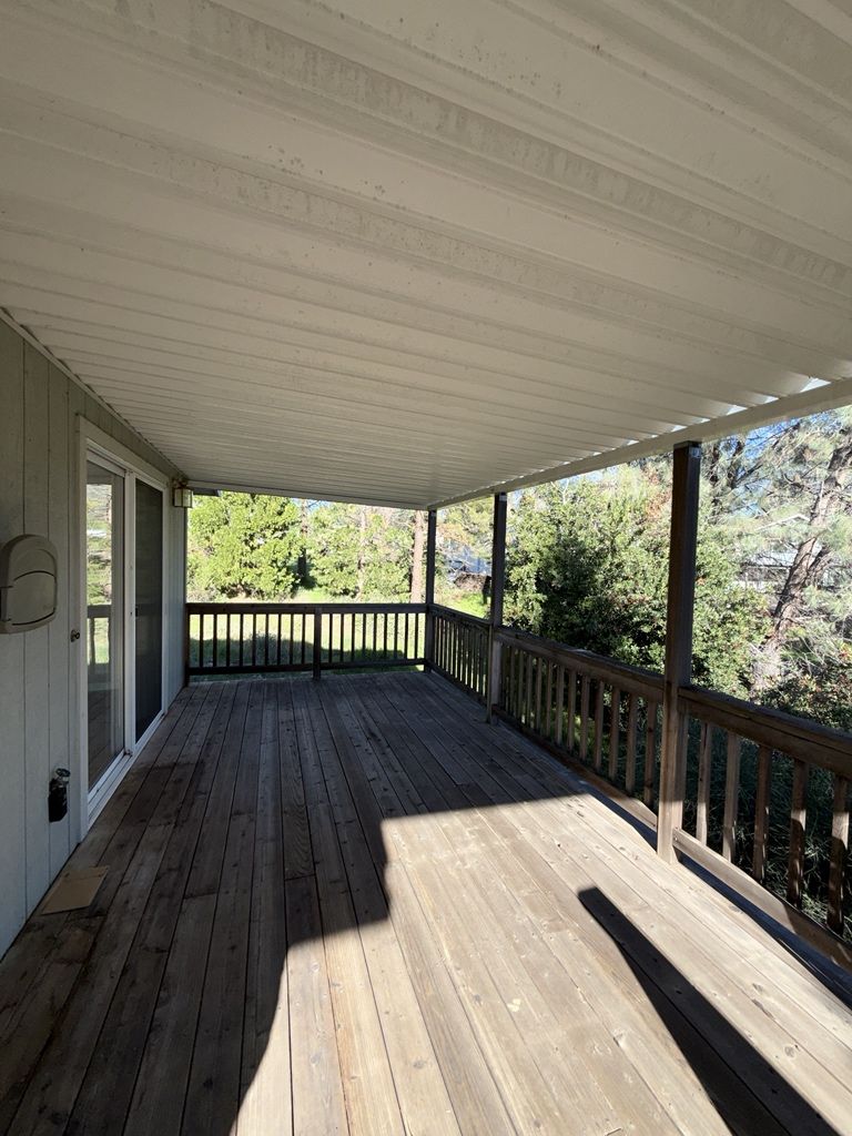 Covered wooden deck with railing, overlooking trees.