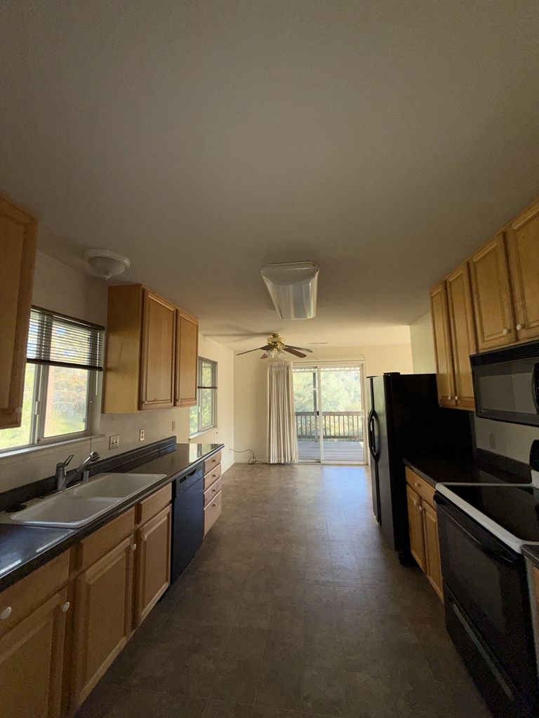 Kitchen with wood cabinets, black appliances, and view of a deck through sliding glass doors.