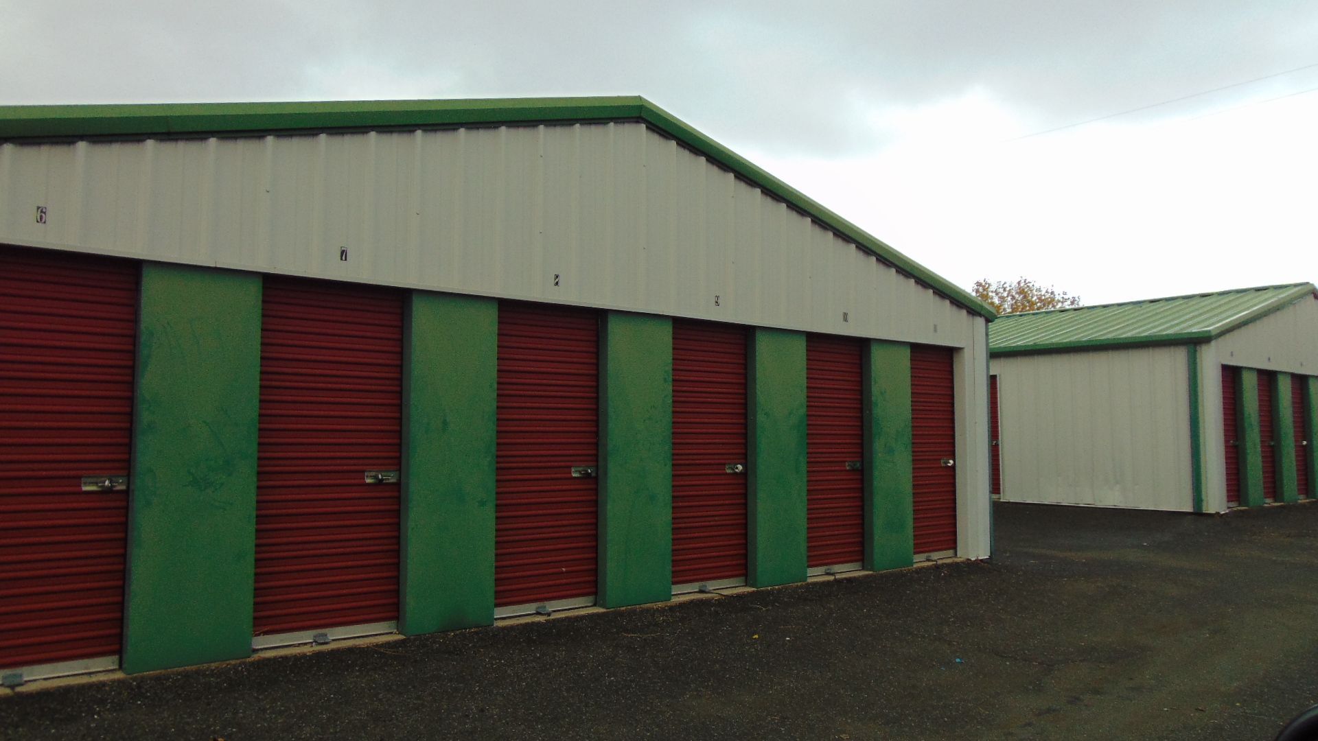 Storage units with red doors and green accents under a cloudy sky.