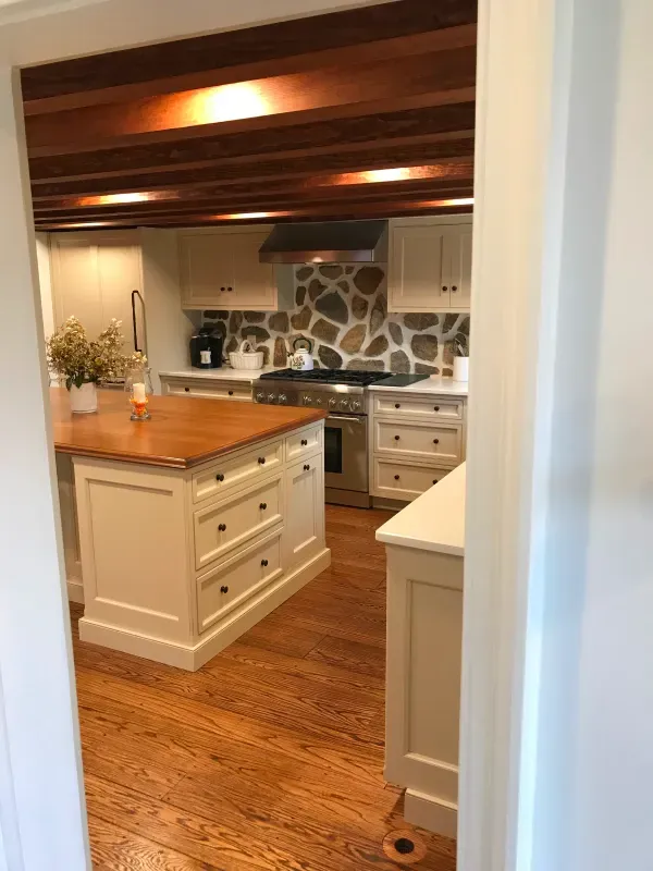 Kitchen with wood floors and ceiling. An island and counters with light-colored cabinets. Stone backsplash.