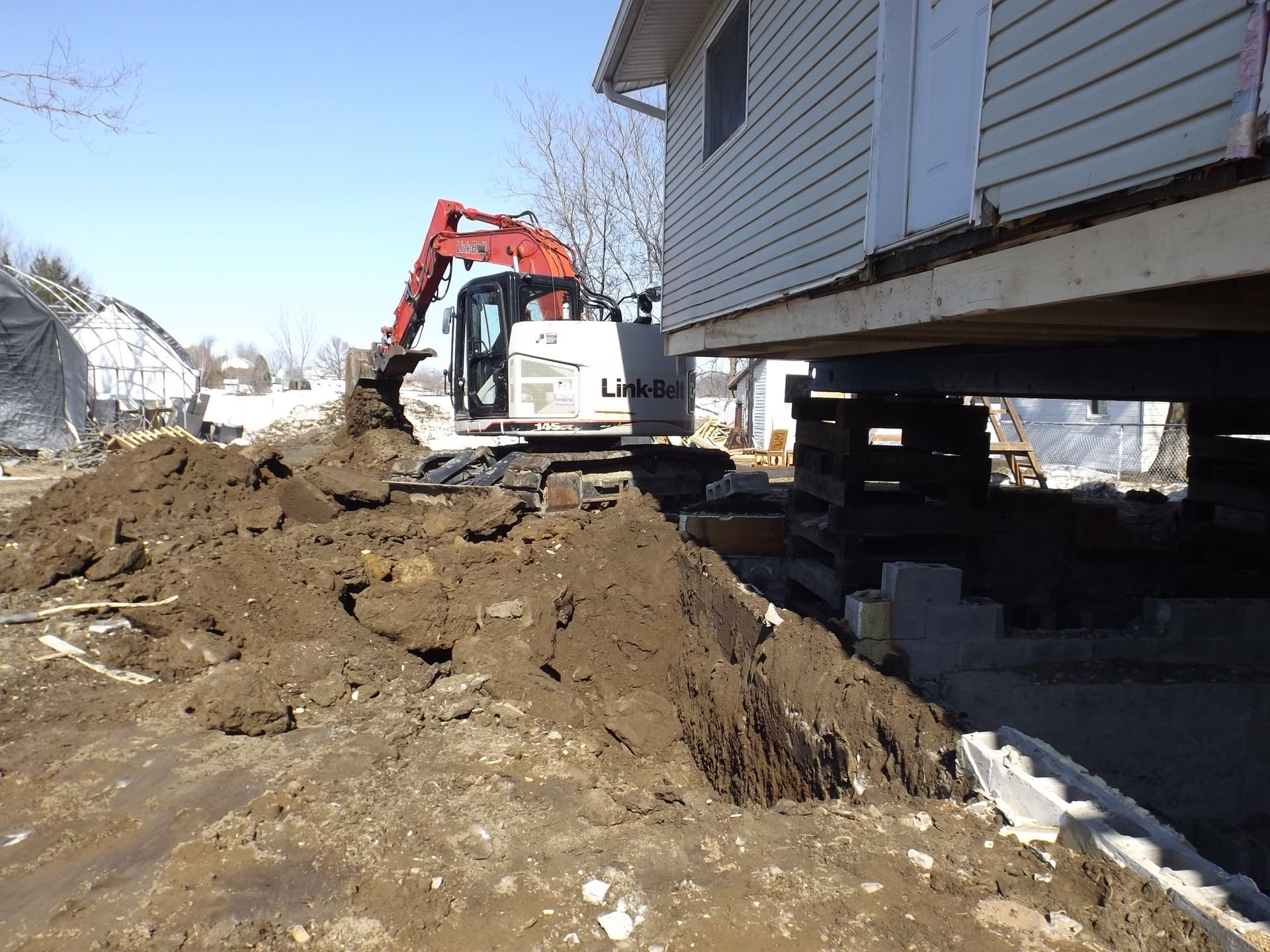 Une excavatrice creuse un trou devant une maison