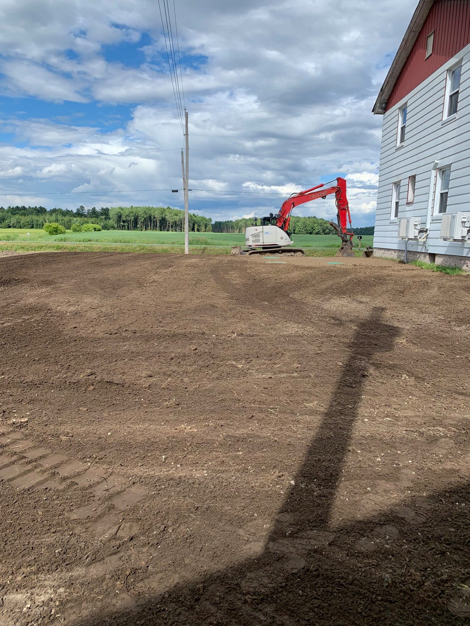 Une excavatrice creuse un trou dans la terre devant une maison.