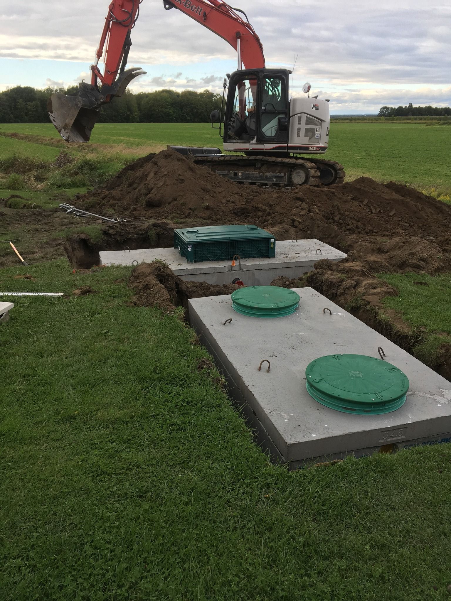 Une excavatrice creuse un trou dans un champ à côté d'une fosse septique.