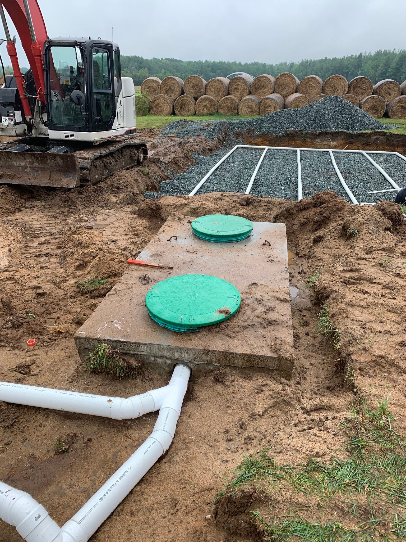 Une fosse septique est en cours d'installation dans un champ de terre avec un bulldozer en arrière-plan.