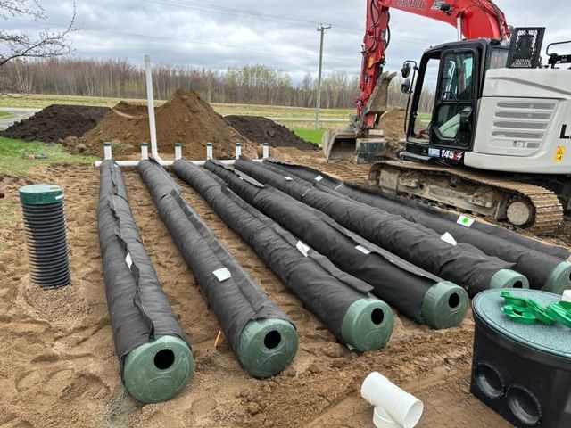 Une grande excavatrice est assise à côté d'un tas de tuyaux dans la terre.