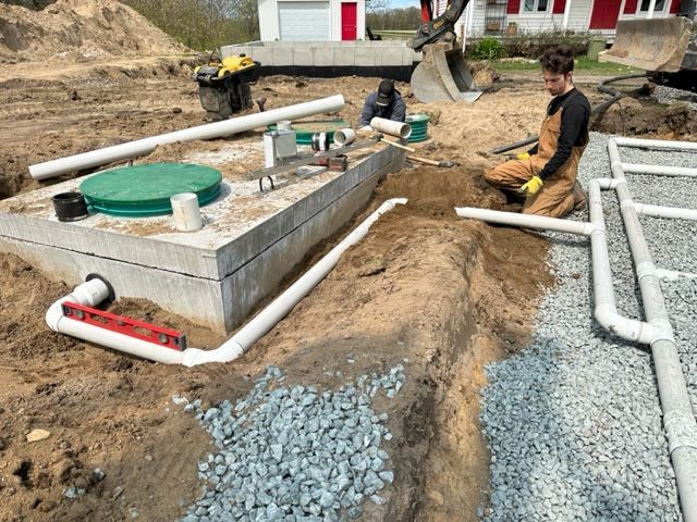 Un homme est agenouillé dans la terre à côté d'une fosse septique.