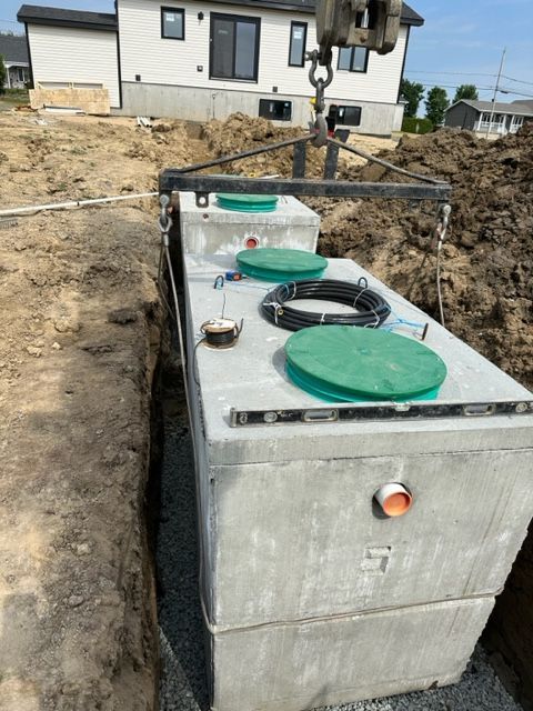 Un grand réservoir en béton avec un couvercle vert est soulevé par une grue.