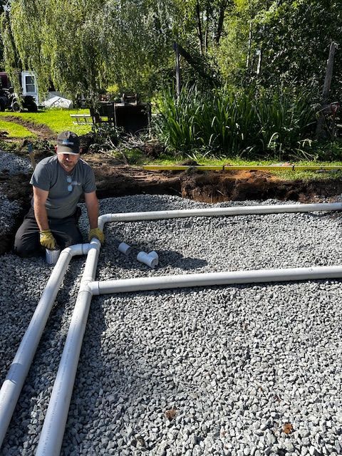 Un homme est agenouillé sur du gravier à côté de tuyaux.