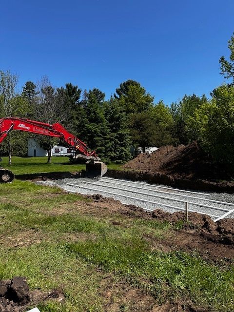 Une excavatrice rouge creuse un trou dans un champ herbeux.