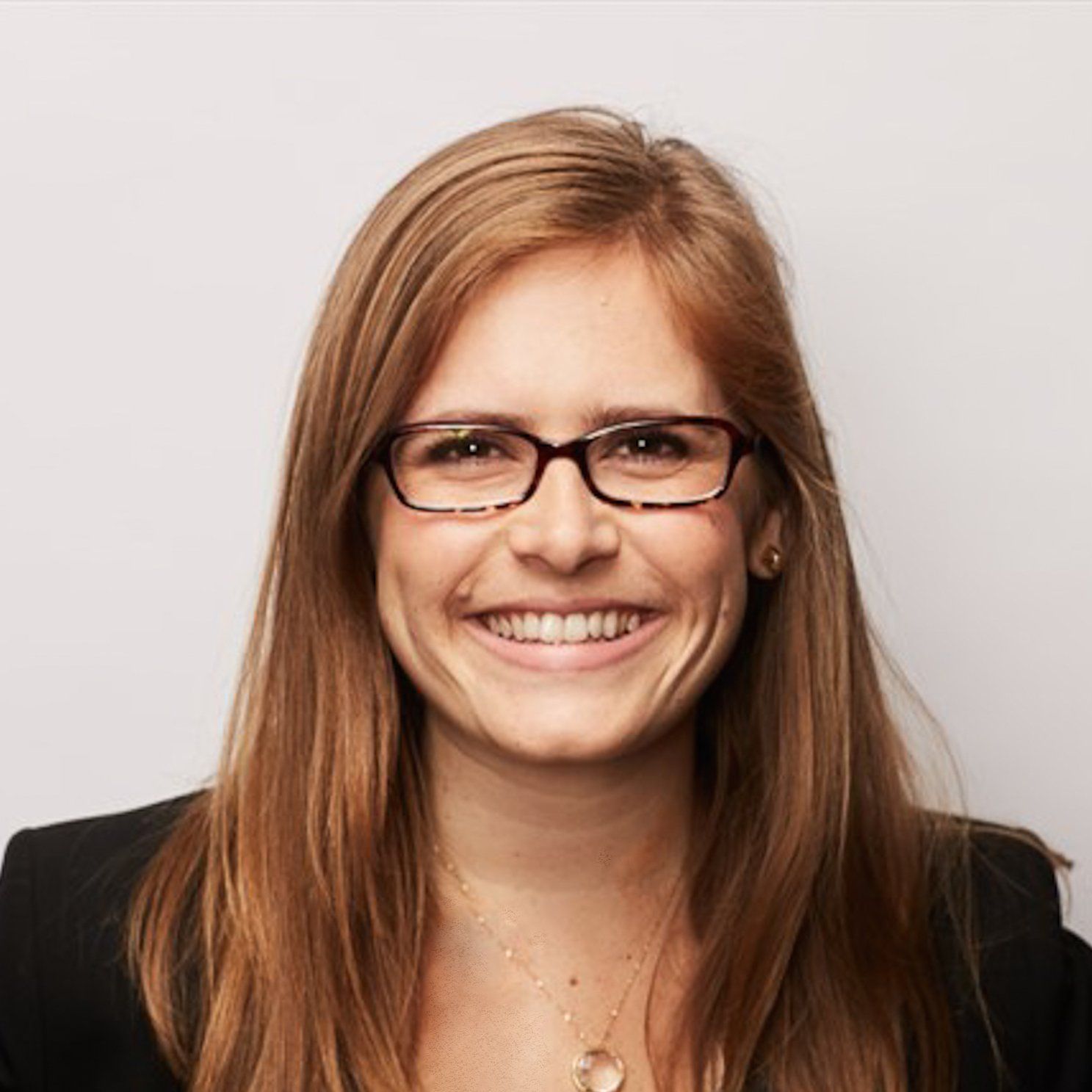 A woman wearing glasses and a necklace smiles for the camera