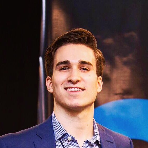 A young man in a suit and plaid shirt is smiling for the camera.