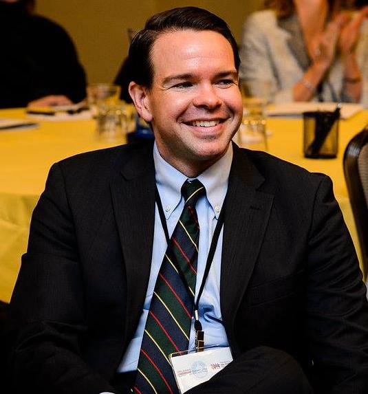 A man in a suit and tie is smiling while sitting at a table