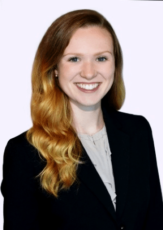 A woman with long red hair is wearing a black jacket and smiling.