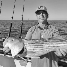 Black and white image of man holding a fish on a boat