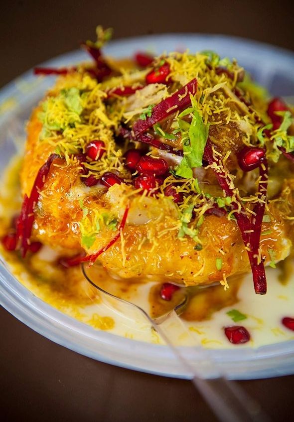 Close-up of a golden-brown, round fried food topped with various garnishes, served in a clear plastic container.
