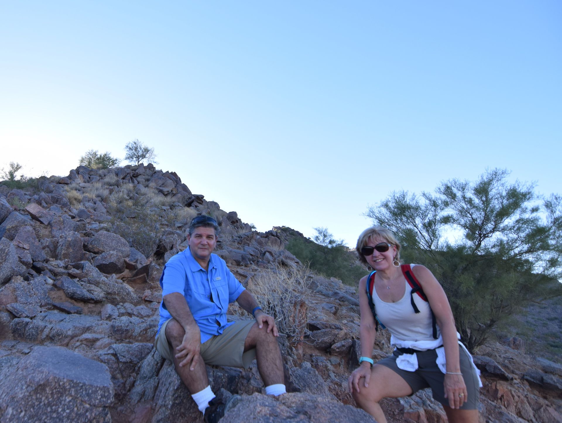 Two people seated on a rocky hillside, man in blue shirt, woman in tank top, both smiling.