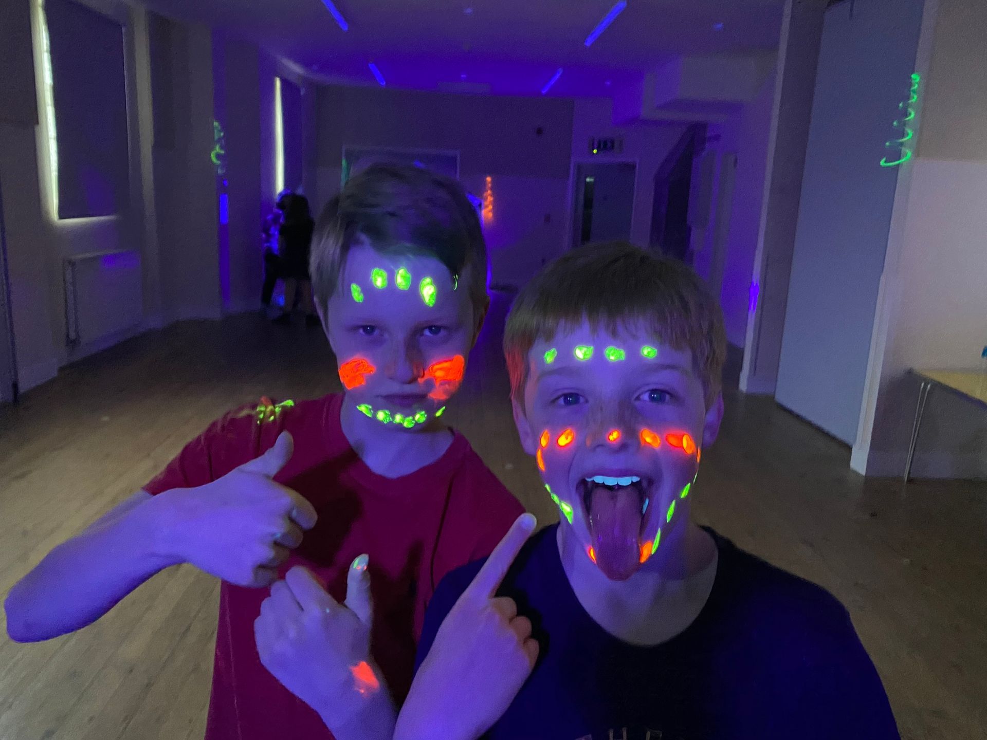 Two boys are standing next to each other with glow in the dark paint on their faces.