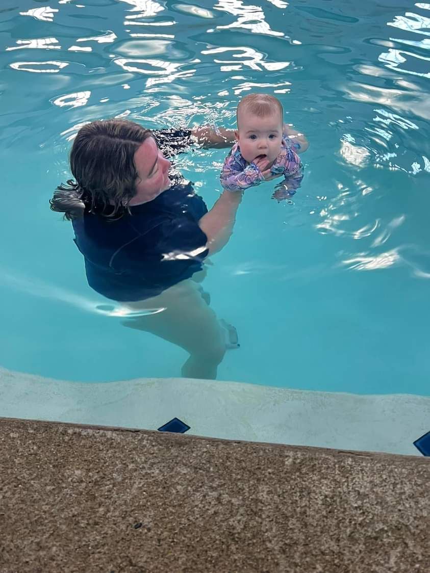 A woman is holding a baby in a swimming pool.
