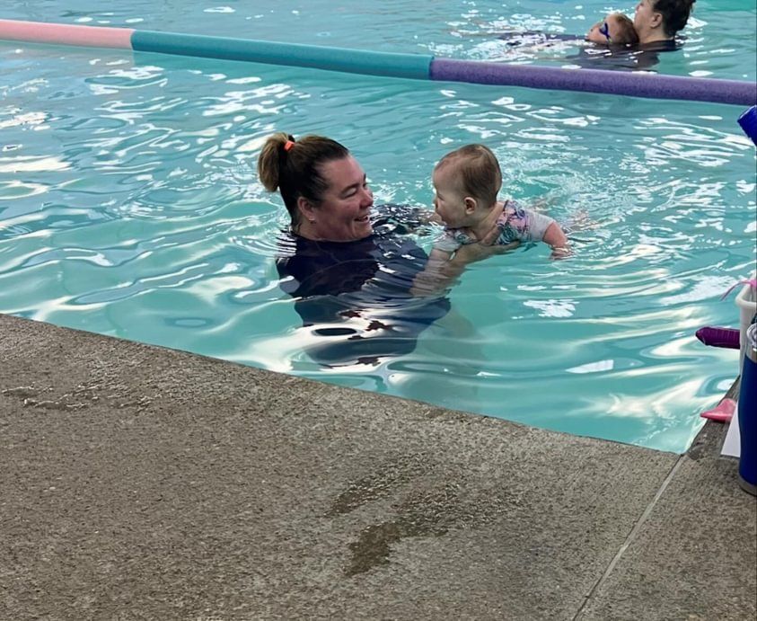 A woman is teaching a baby how to swim in a swimming pool.