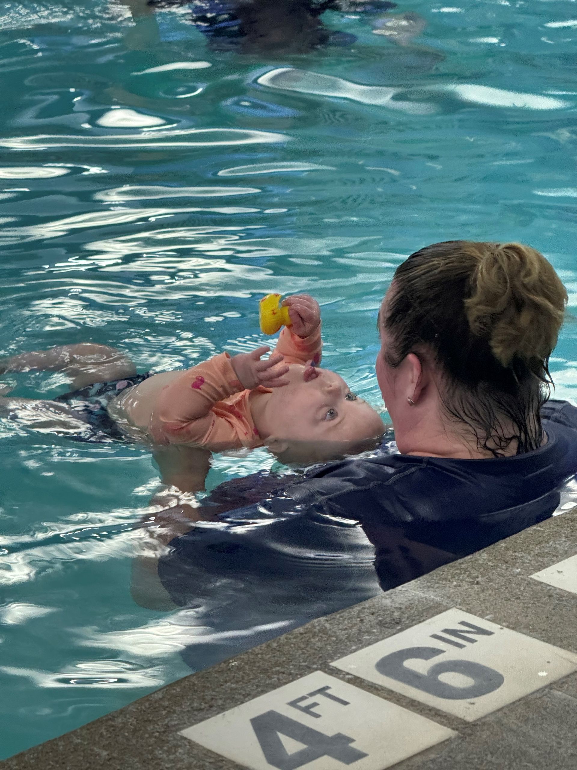 A woman is holding a baby in a swimming pool that is 4 ft 6 in