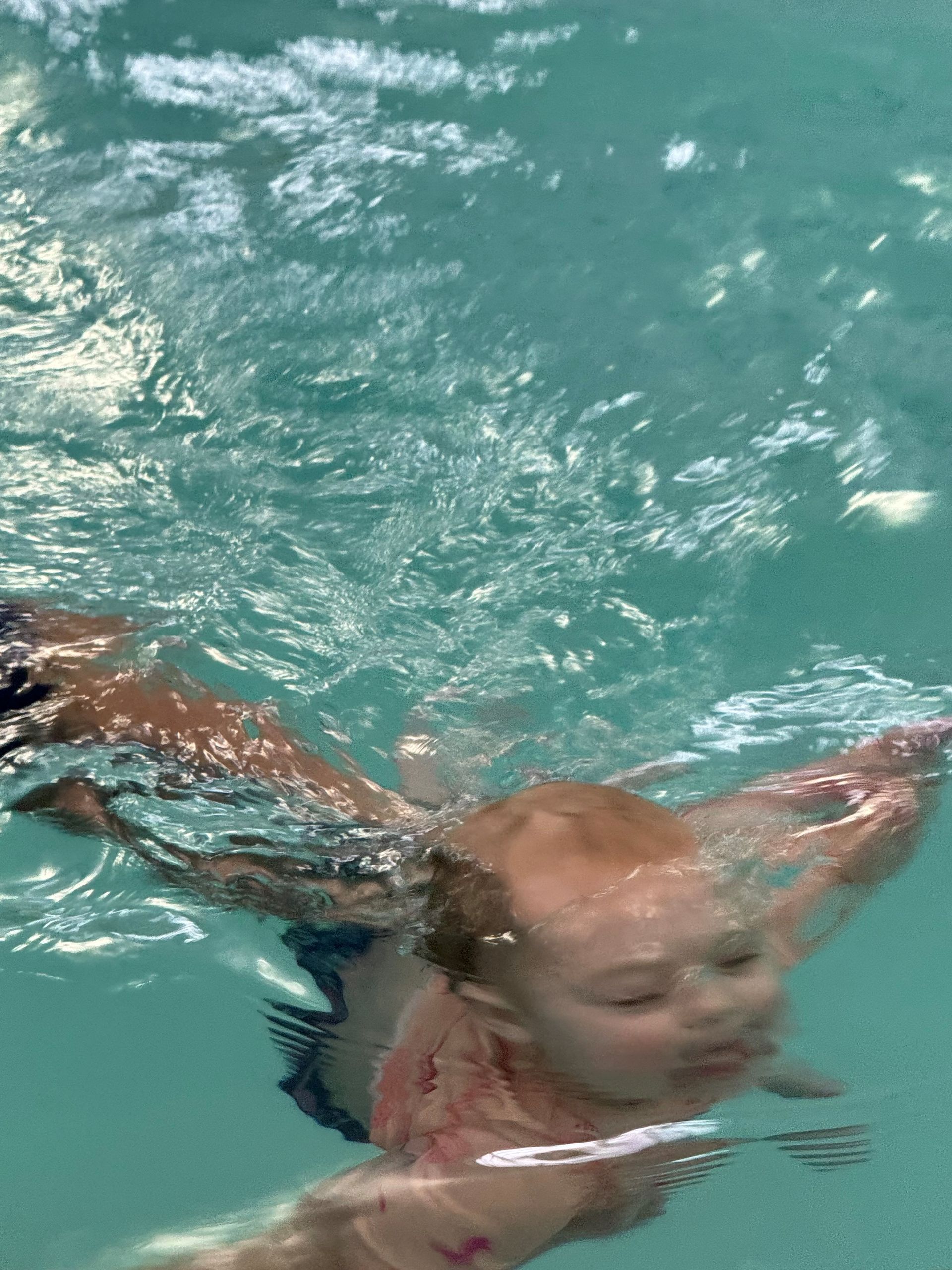 A baby is swimming underwater in a pool.