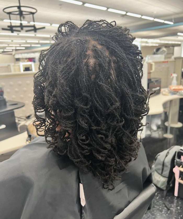 Back view of a person with short, curly micro locs. They are in a salon setting.