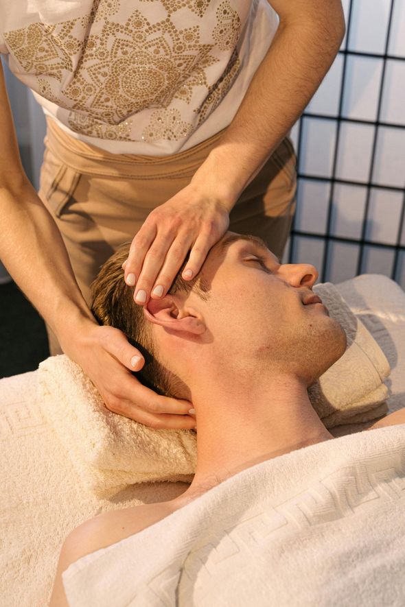Man receiving head massage at a spa; masseuse's hands on his head.