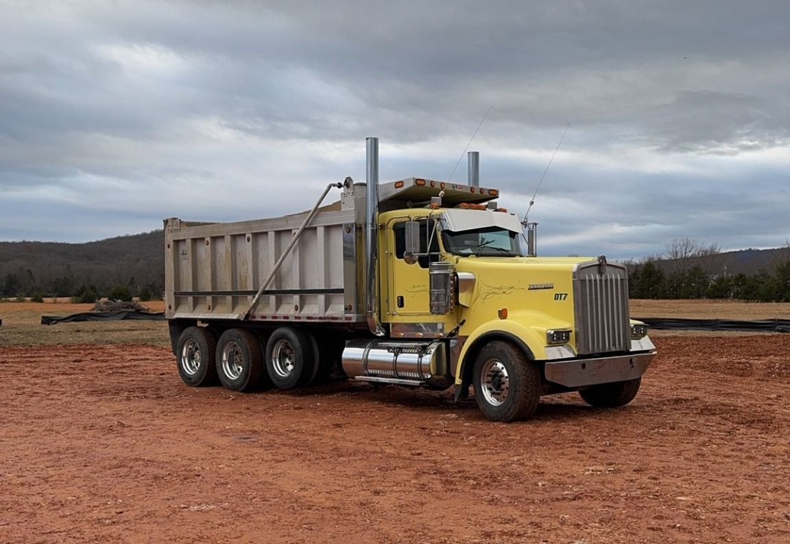 Yellow dump truck on a dirt road under a cloudy sky.