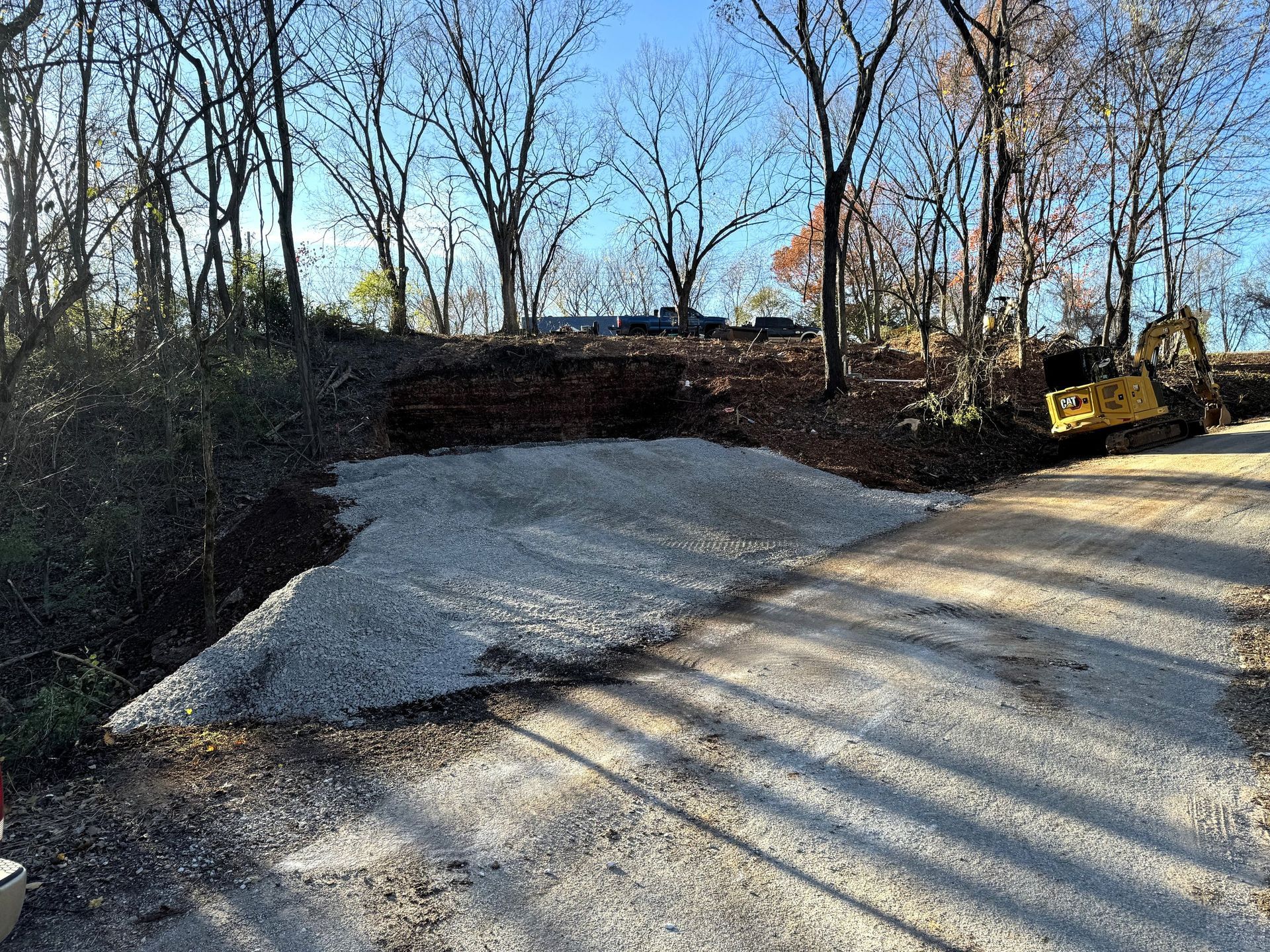 Gravel pile and construction equipment adjacent to a road with leafless trees in background.