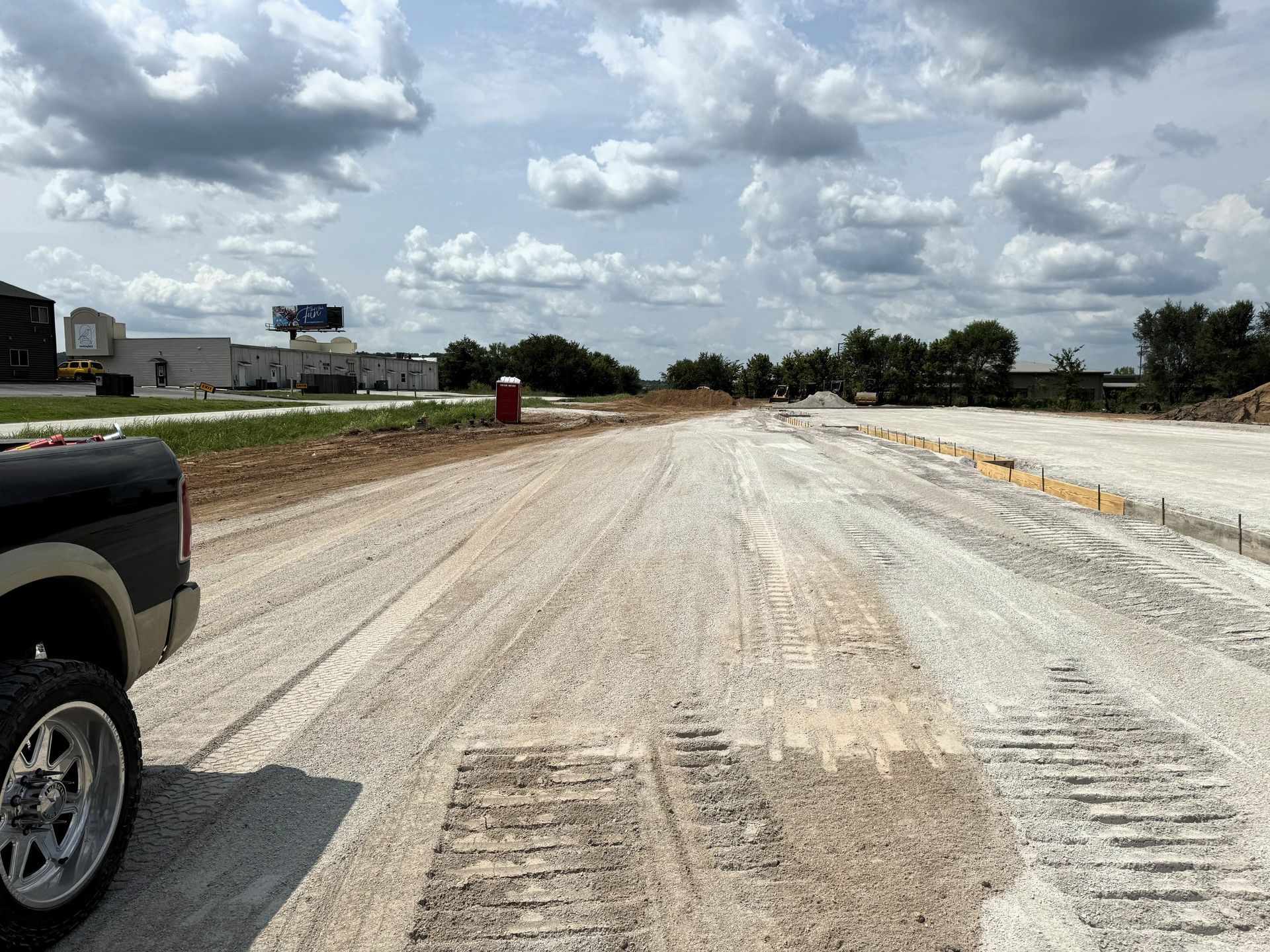 Construction site with a dirt road, portable toilet, and cloudy sky. A truck is on the left.
