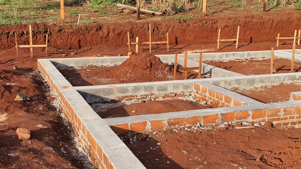 Foundation of a building under construction, with brick and cinder block walls on reddish earth.