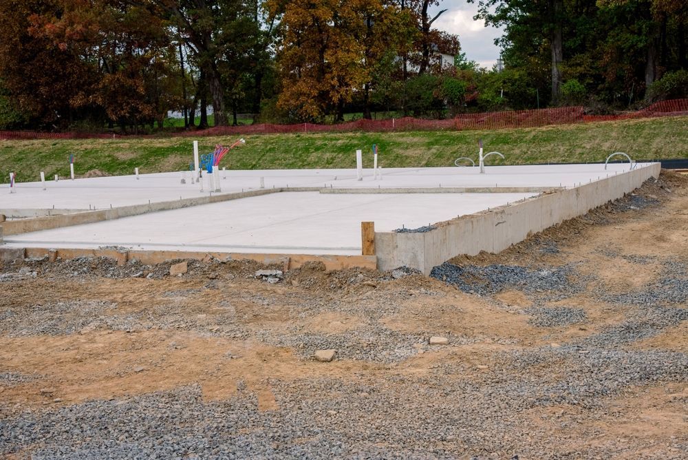 Concrete foundation for a building in a dirt lot, with plumbing pipes.