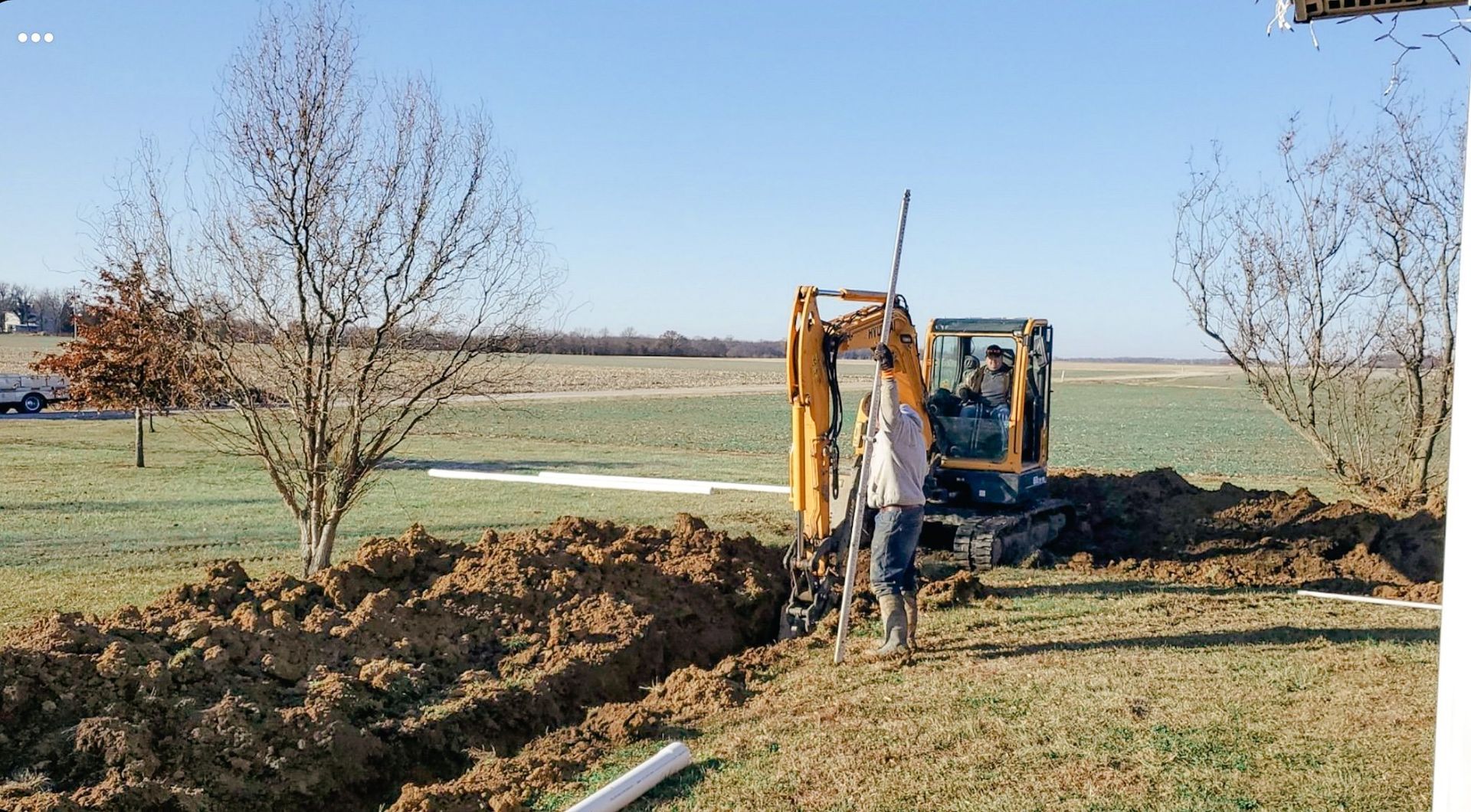 A man is driving a yellow excavator in a field.