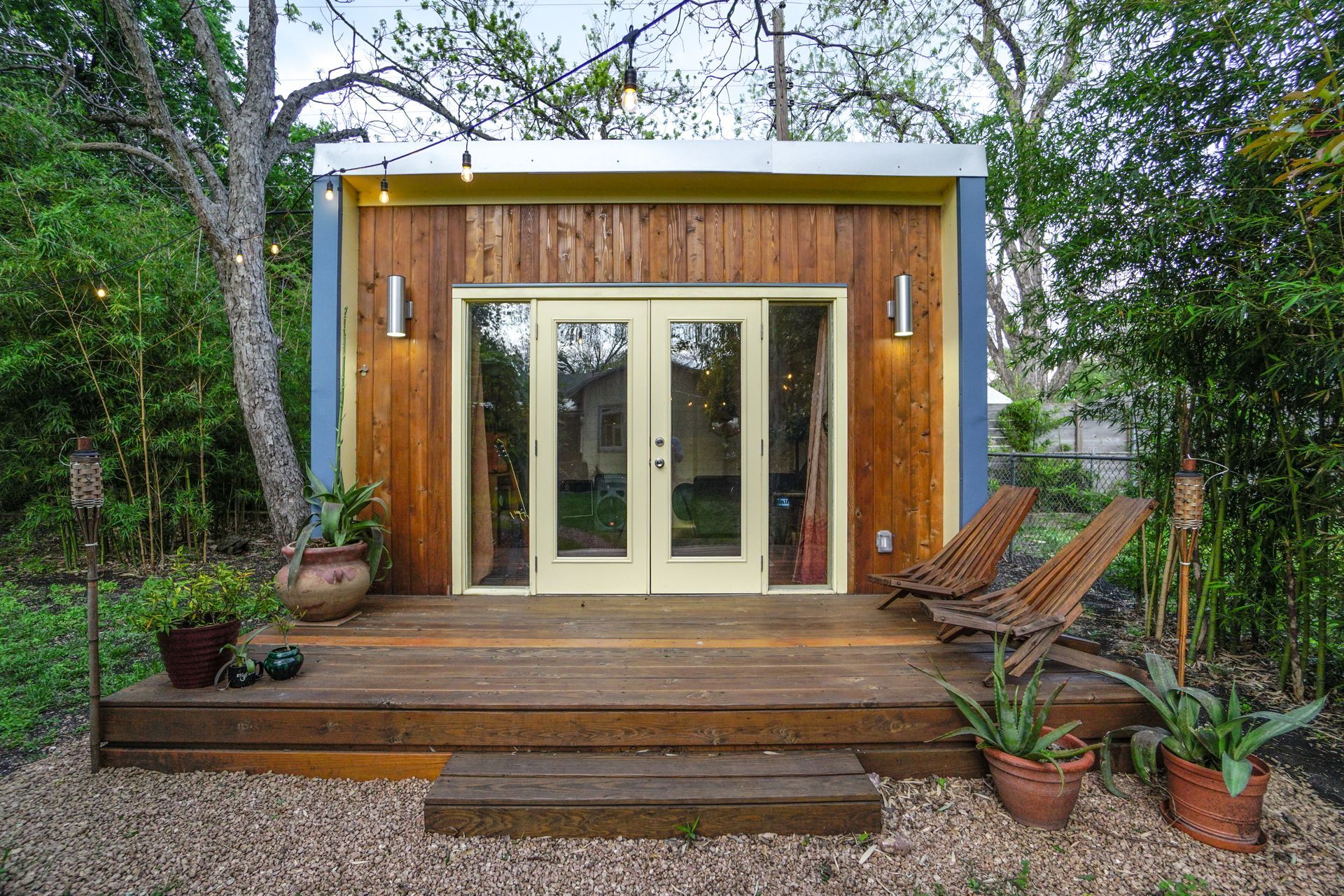 Wooden backyard office with deck, French doors, wood siding, and surrounding trees.