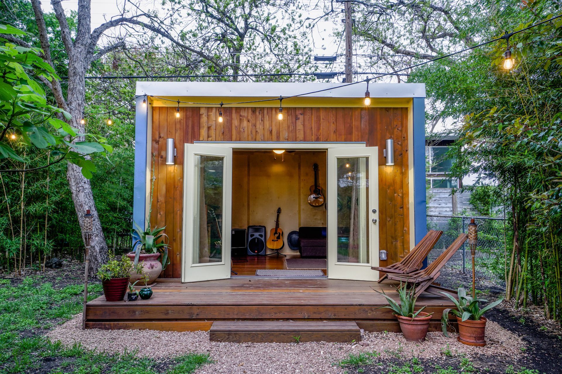 Small backyard studio with wooden siding, open French doors, and string lights.