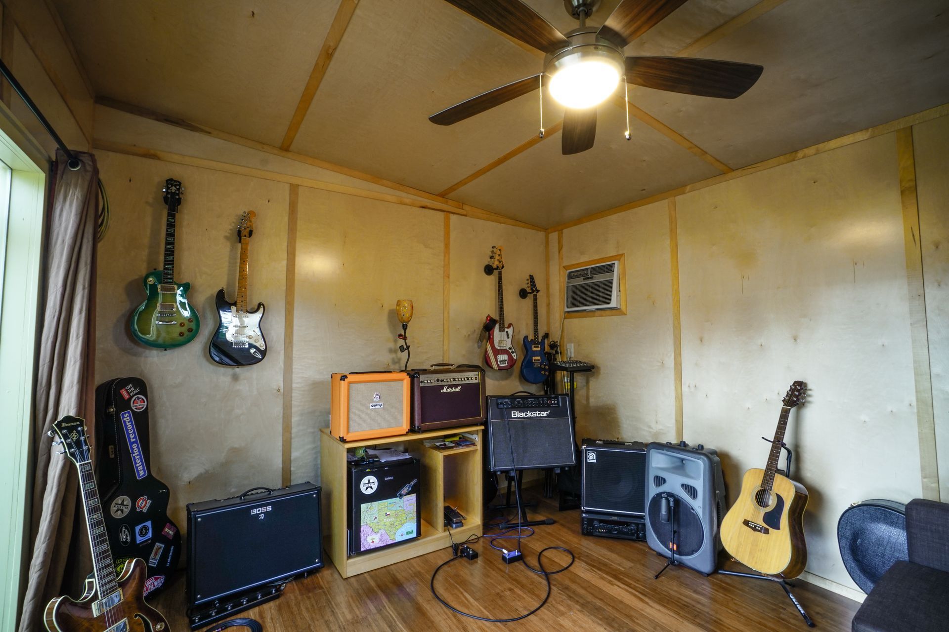 A music room with guitars on walls, amplifiers, and a ceiling fan.