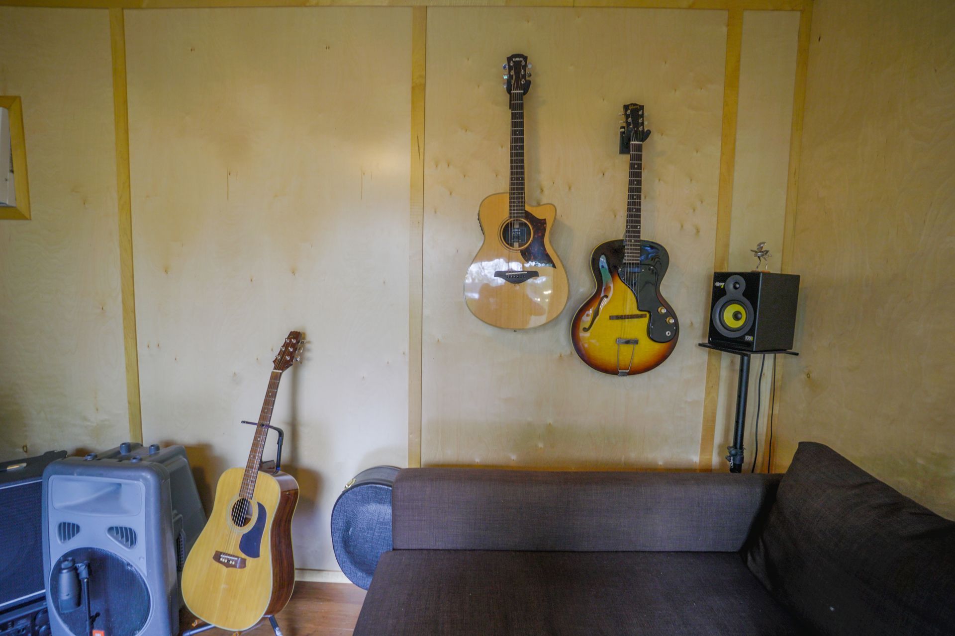 Guitars on wall and stand, speaker, couch, and amplifier in room.