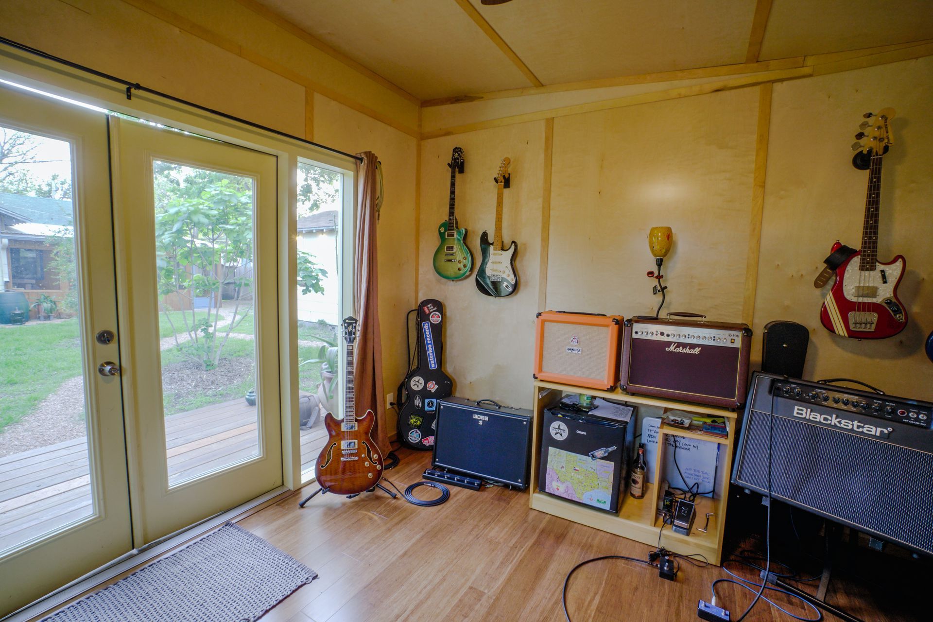 Music room with guitars, amplifiers, and French doors leading to a yard.
