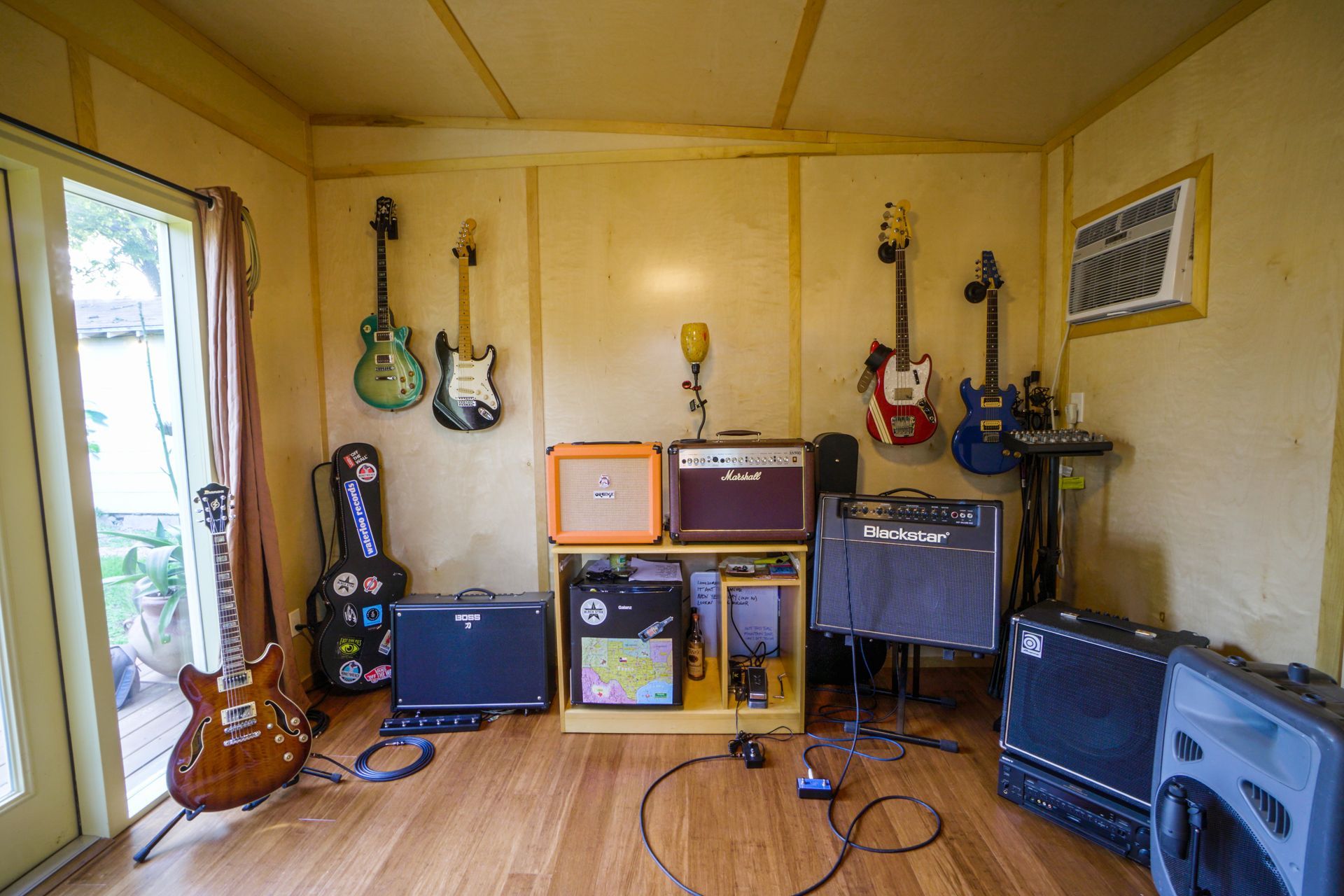 Music studio with guitars on walls, amps, and a guitar leaning against a door.