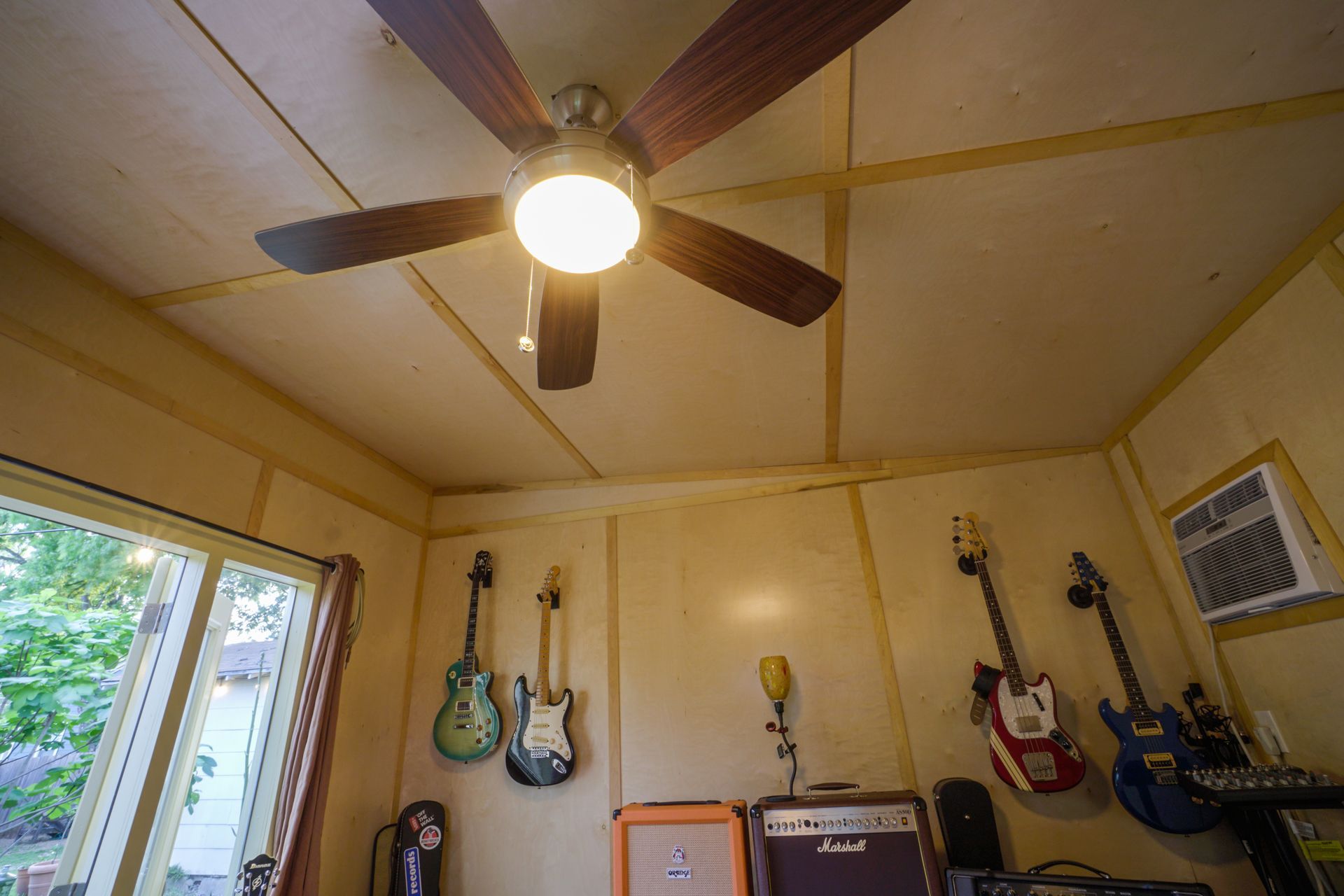 Ceiling fan with light in a room with guitars, an amplifier, and a window.
