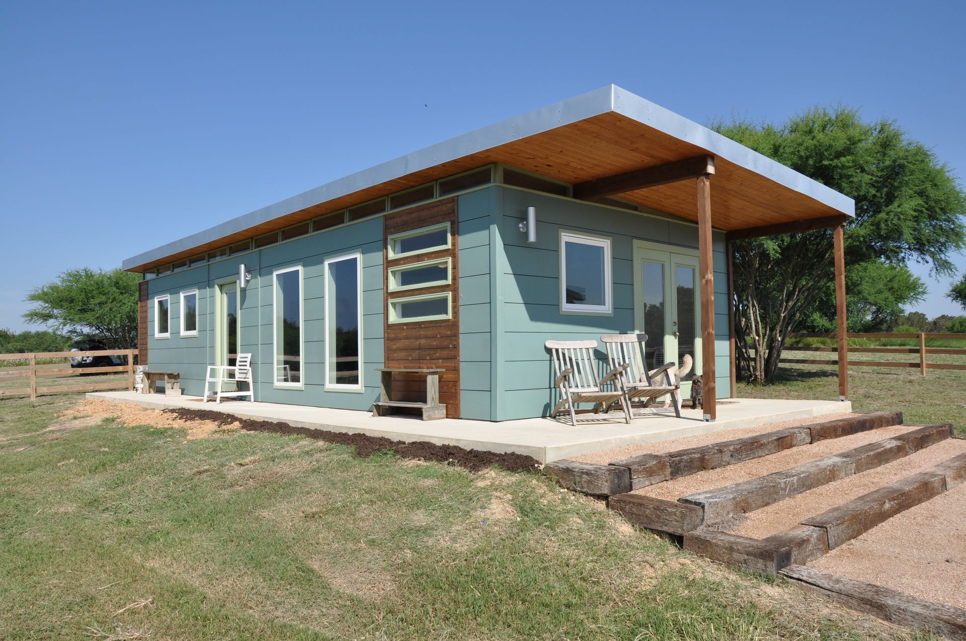 Modern tiny house with wood porch and steps in a grassy field