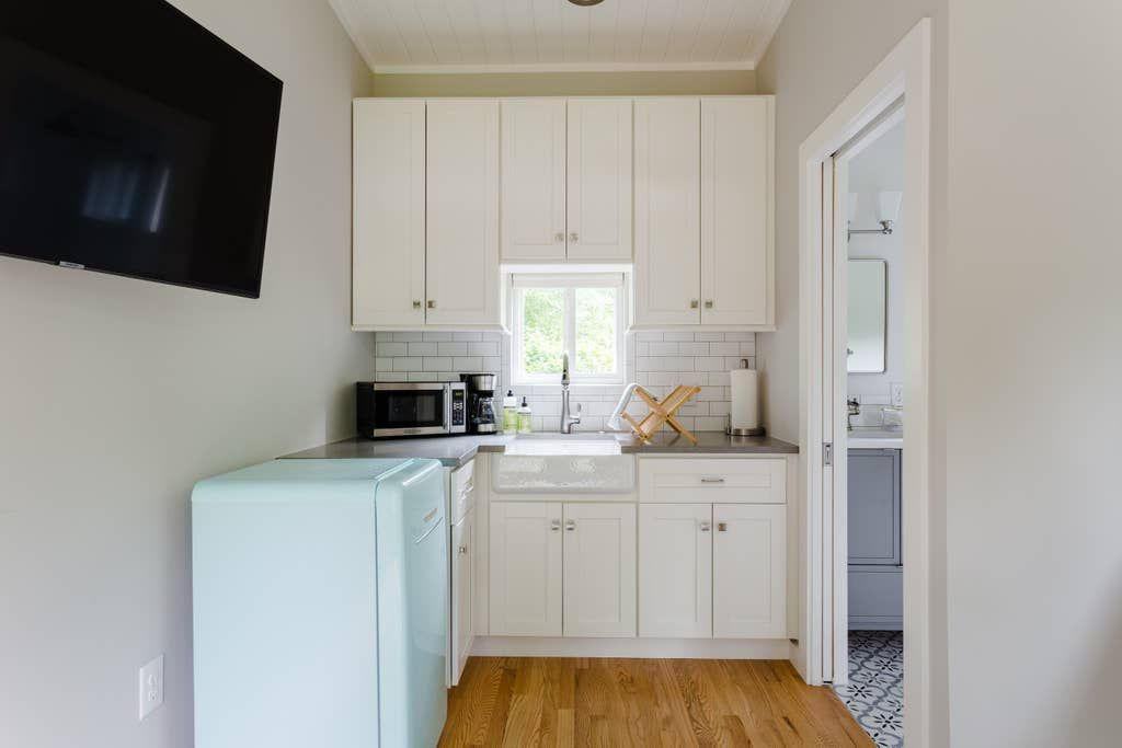 Small kitchen with white cabinets, a light blue fridge, and a view into a bathroom.