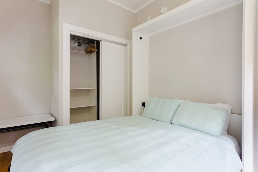 Bedroom with a made bed, closet with sliding doors, and a wall-mounted bed frame.