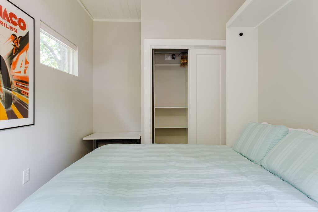 Small bedroom with bed, closet, art, and a small window.