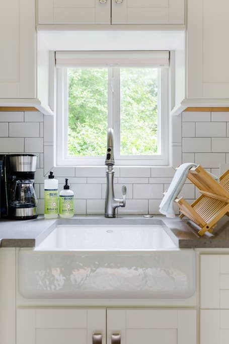 Kitchen sink with a window above it, surrounded by white cabinets and subway tile.