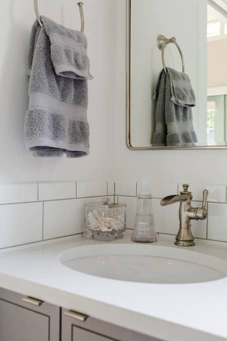 Bathroom sink with gray towels, mirror, and countertop accessories.